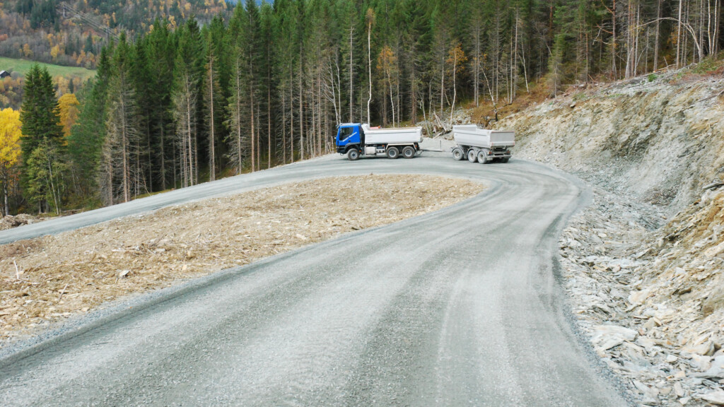 Lastebil med henger som kjører i en sving på en skogsbilveg. Foto.