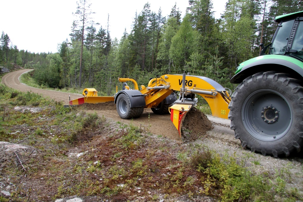 Traktor som skraper en skogsbilvei med en slepehøvel. Foto.